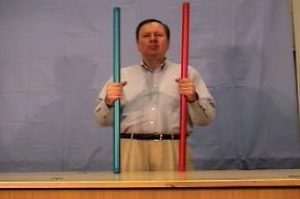 The instructor holds two rods of identical size and weight, one red and one blue.